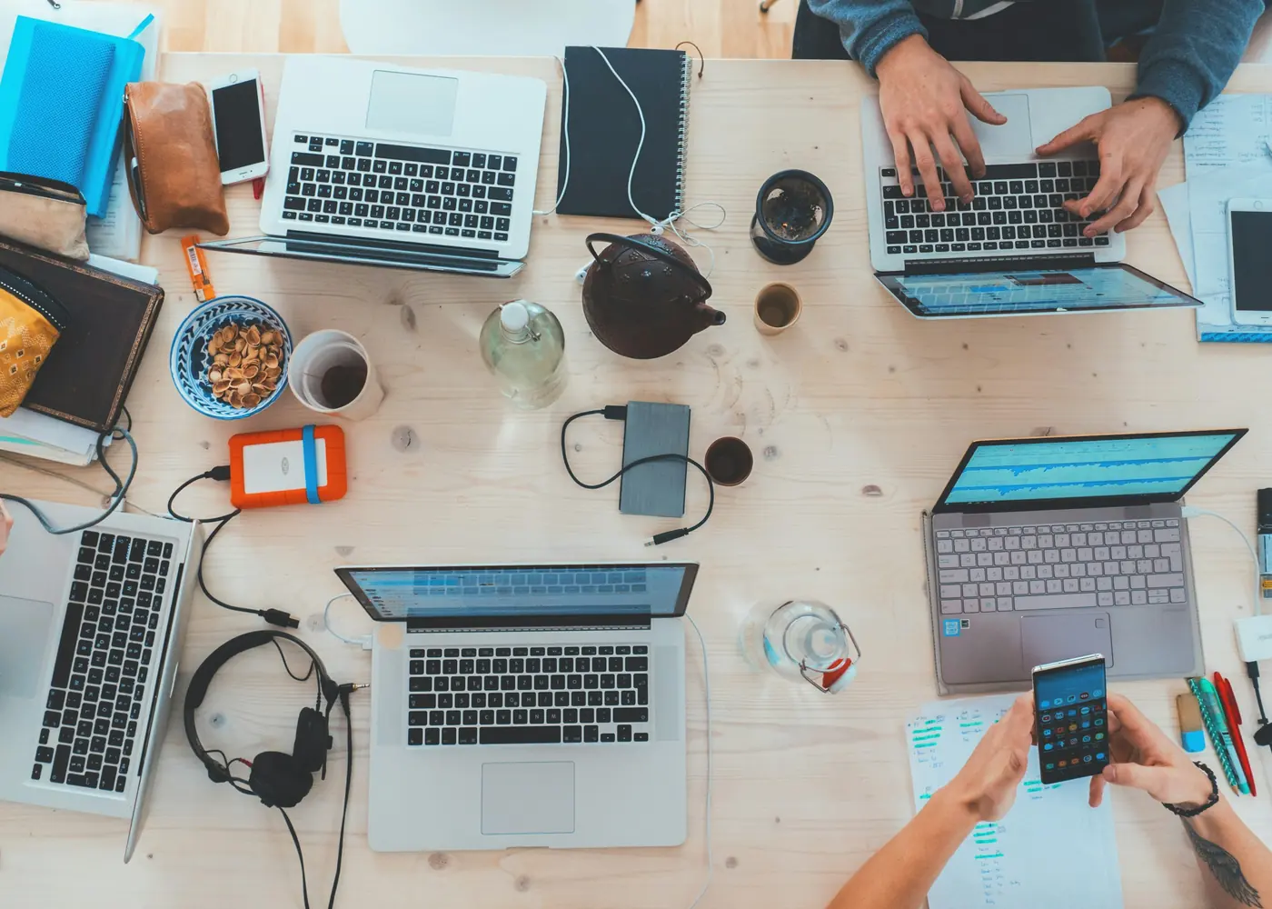 A shared desk seen from above with laptops, notebooks and coffee